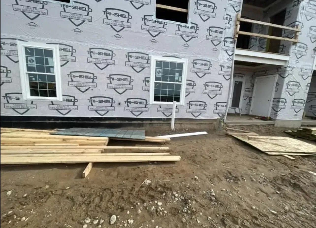 Two new white double-hung windows set and trimmed on house wrap